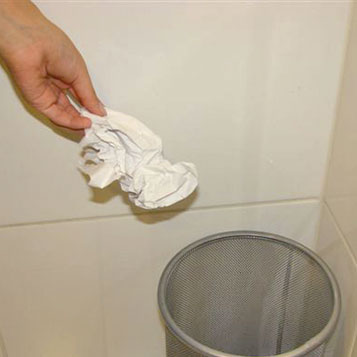 Mano botando toalla de papel usada a un basurero
