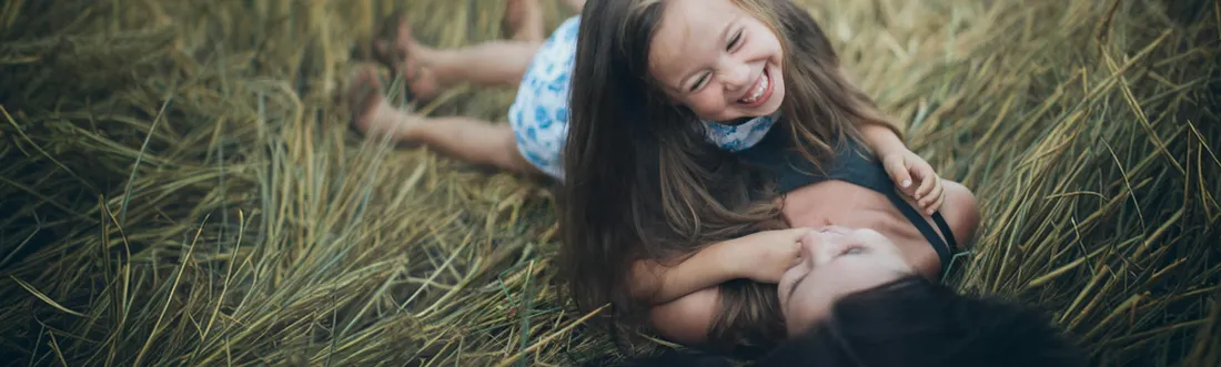 Madre e hija riendo recostadas en un campo de trigo