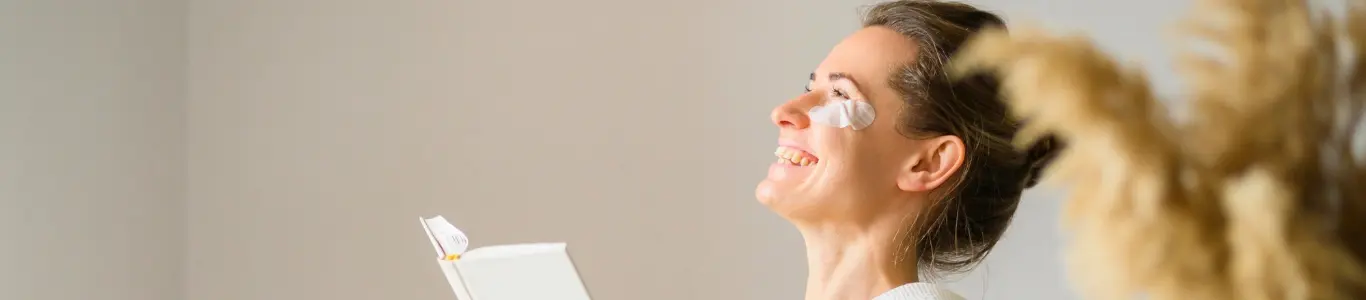 Persona sonriendo con parches faciales y libro en mano, imagen de autocuidado y bienestar para enfrentar el agotamiento de fin de año.