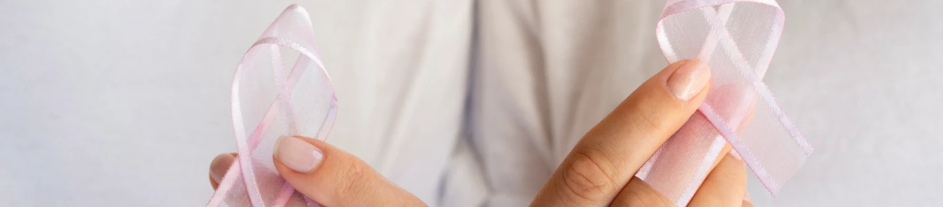 Lazos rosados en las manos, representando apoyo y conciencia sobre la detección temprana del cáncer de mama.