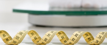 Cinta métrica enrollada frente a una balanza digital, simbolizando cómo subimos de peso y la importancia de contar con un seguro Alemana  Salud para el bienestar integral.