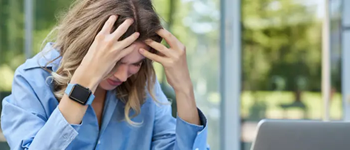 Mujer con signos de estrés y agotamiento frente al computador, imagen relacionada con el impacto del estrés en la salud física y mental.