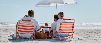 Familia disfrutando de la playa bajo una sombrilla en un día soleado, representando el ideal de unas vacaciones seguras en compañía, protegidos con un seguro de accidentes.