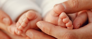 Manos de adulto sosteniendo los pies de un recién nacido, reflejando el cuidado de la salud del recién nacido y la protección que entrega el seguro  Salud.