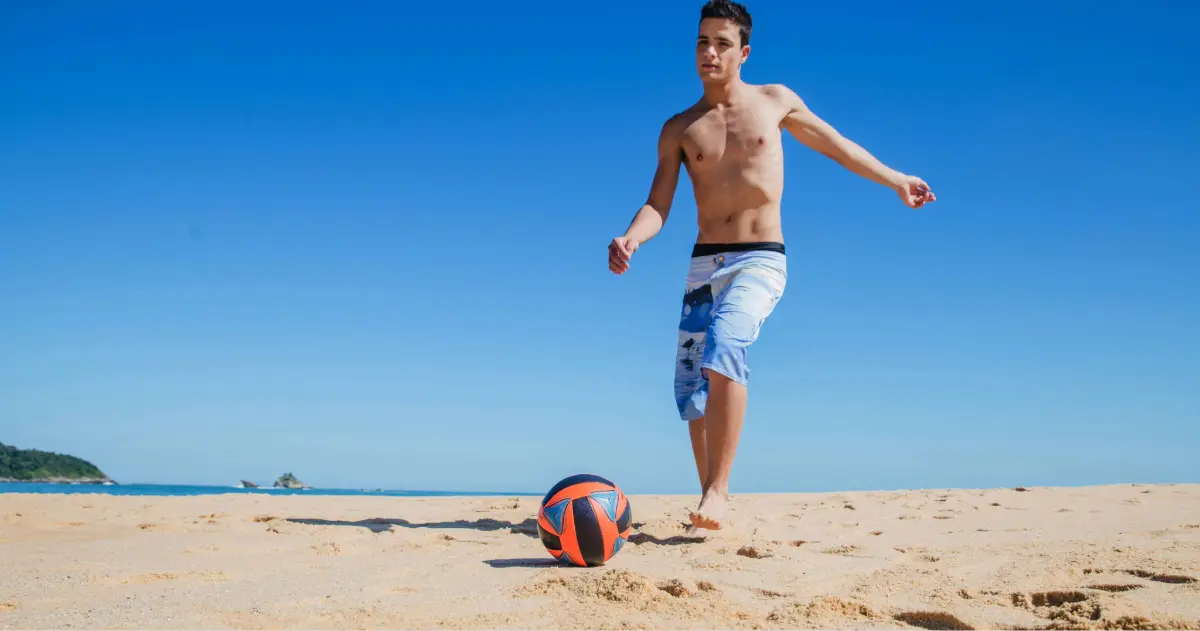 Persona practicando fútbol en la playa, imagen asociada a la protección y coberturas de un seguro de accidentes.