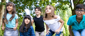 Grupo de niños jugando al aire libre en un parque, sonrientes y activos, bajo árboles.