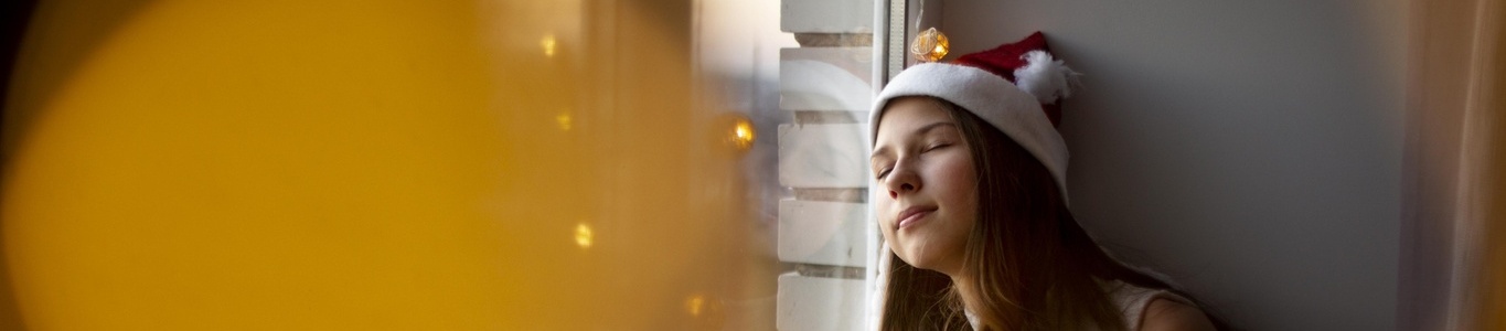 Joven con gorro navideño descansando sola junto a la ventana en una escena de Navidad solitaria.